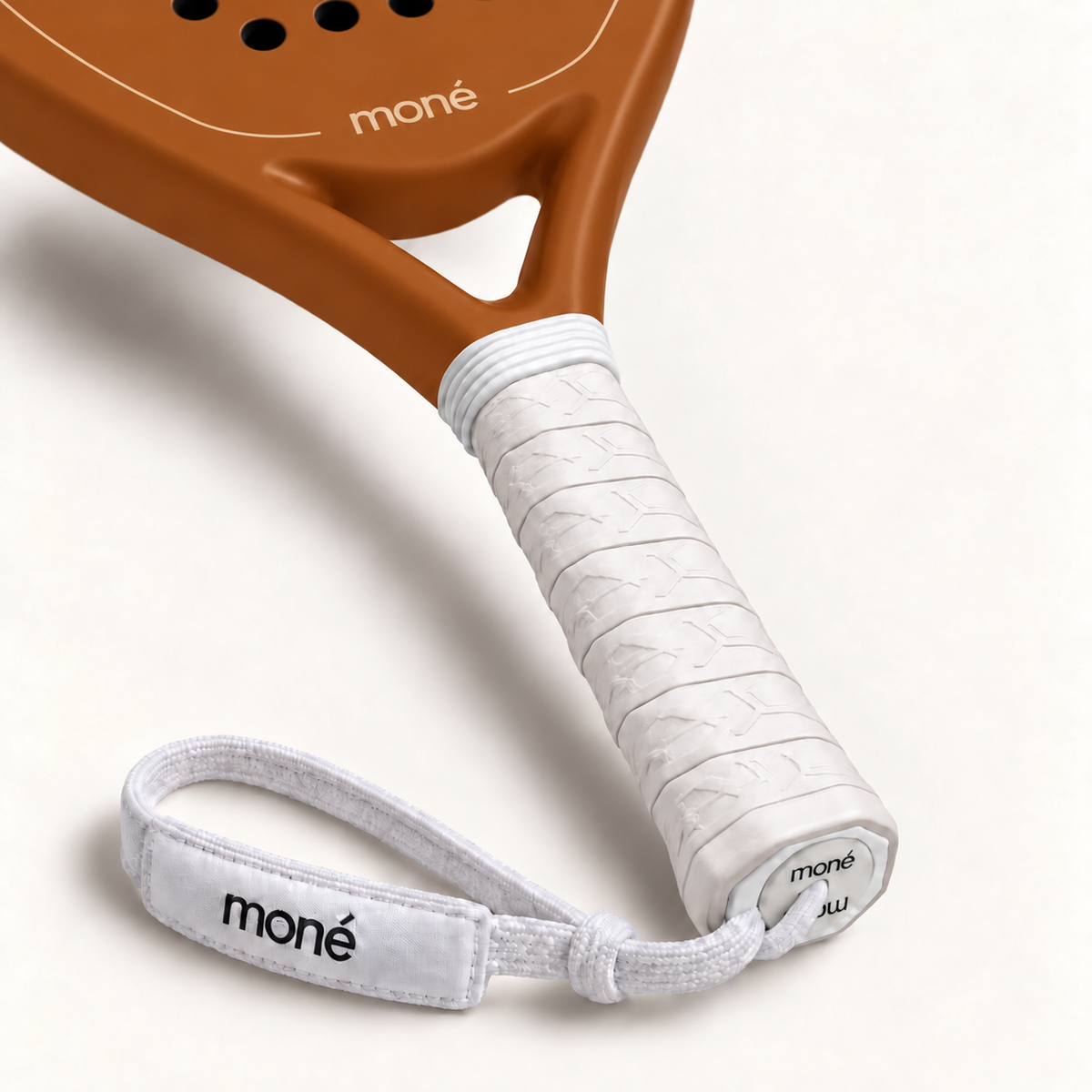White textured grip, logo end cap and moné wrist strap on the Sienna light brown padel racket, close-up