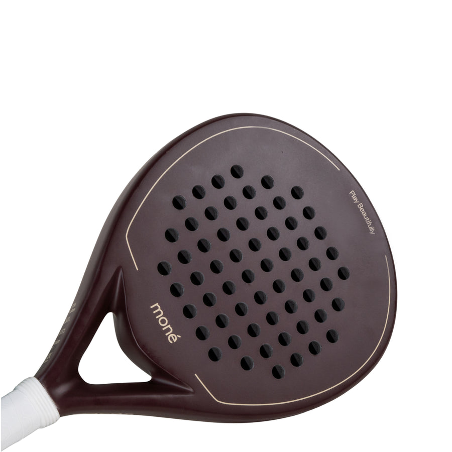 Detailed surface view of the Moné Padel Cocoa premium racket showing teardrop hole pattern and dark finish.