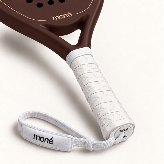 White textured grip, logo end cap and moné wrist strap on the Cocoa brown padel racket, close-up