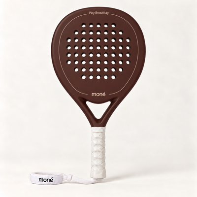 Cocoa brown padel racket by moné, front view with Play Beautifully lettering, a white grip and moné wrist strap