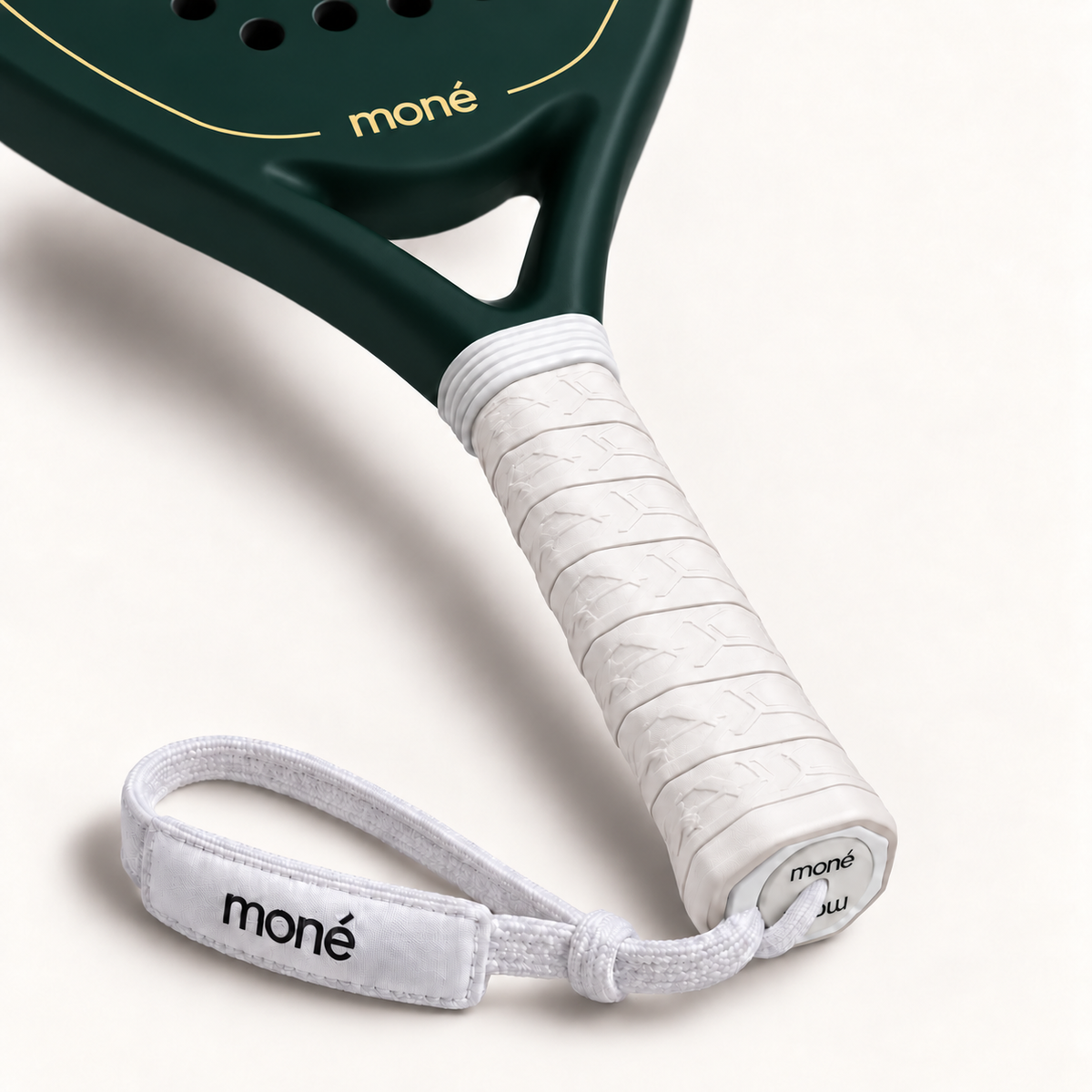 White textured grip, logo end cap and moné wrist strap on the Forest dark green padel racket, close-up