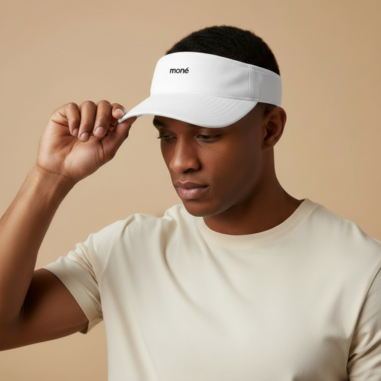 Person wearing a white visor with 'moné' branding on a beige background. Court Visor - White | Moné Padel