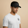 Man wearing a white t-shirt with a logo and a black visor on a beige background. Court Visor - Black | Moné Padel
