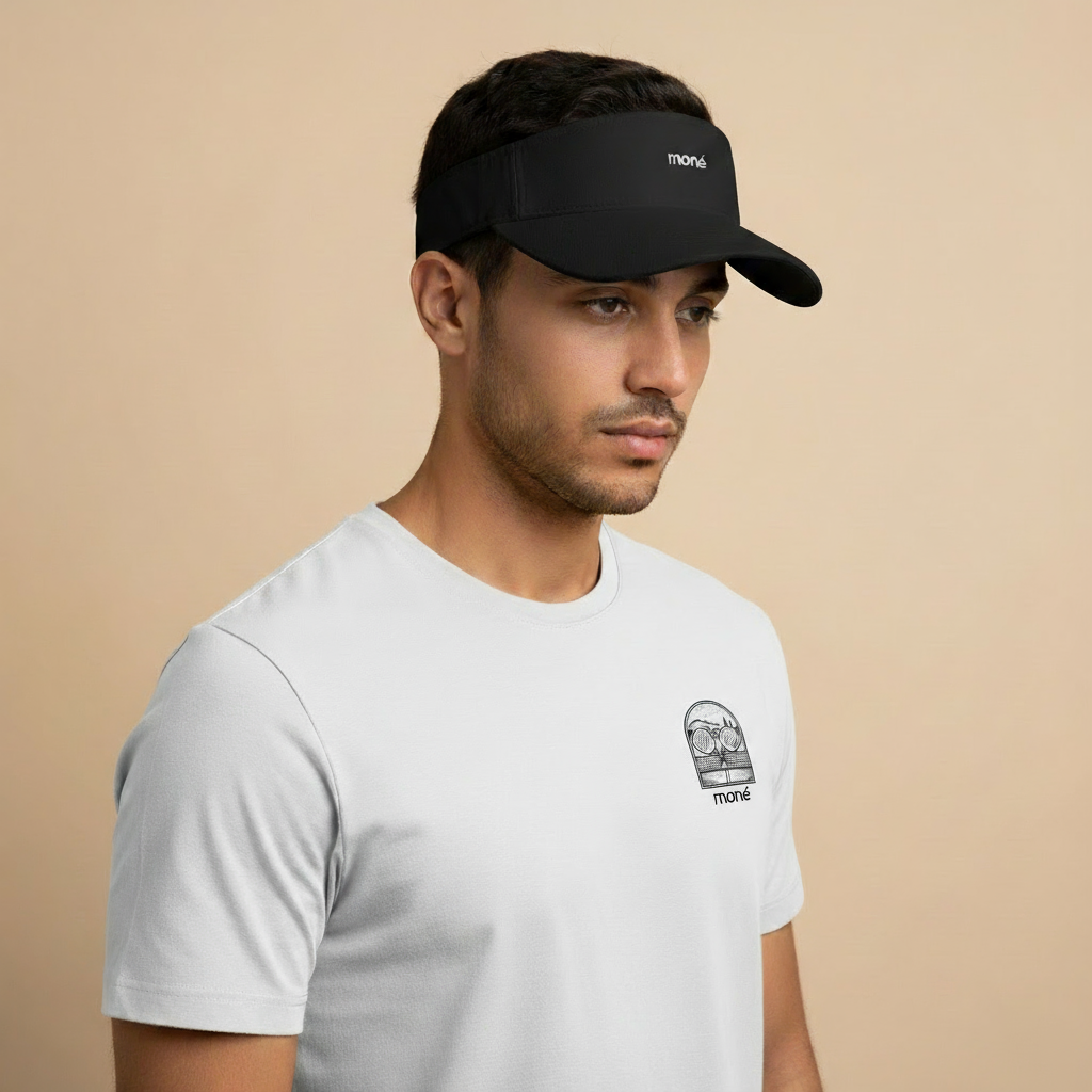 Man wearing a white t-shirt with a logo and a black visor on a beige background. Court Visor - Black | Moné Padel
