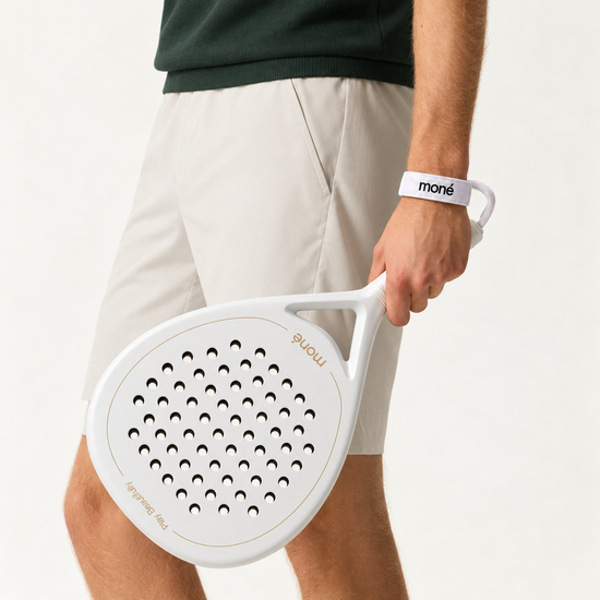 Man in beige shorts and a dark green knit holds the off-white Ivory Hybrid padel racket by his side