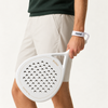 Man in beige shorts and a dark green knit holds the off-white Ivory Hybrid padel racket by his side