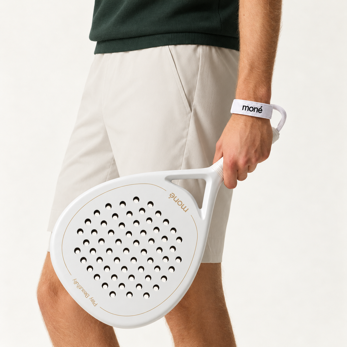 Man in beige shorts and a dark green knit holds the off-white Ivory Hybrid padel racket by his side