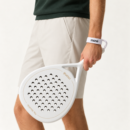 Man in beige shorts and a dark green knit holds the off-white Ivory Hybrid padel racket by his side
