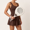Woman in a brown tennis dress holds the off-white Ivory Hybrid padel racket, a moné strap around her wrist