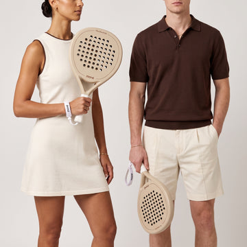 Woman in a cream dress and man in a brown knit polo each hold the beige Sahara Hybrid padel racket
