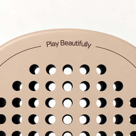 Play Beautifully printed in cocoa brown at the top of the Sahara beige padel racket, above its drilled hole pattern