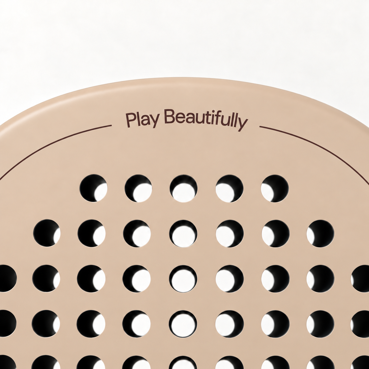 Play Beautifully printed in cocoa brown at the top of the Sahara beige padel racket, above its drilled hole pattern