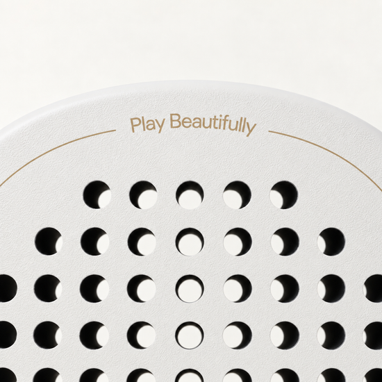 Play Beautifully in gold lettering across the top of the off-white Ivory Hybrid padel racket face and holes