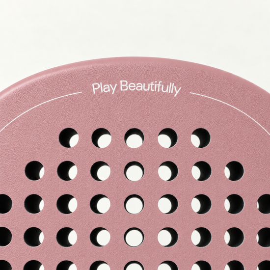 Top of the pink Himalaya Hybrid padel racket face, with Play Beautifully printed in white above the holes