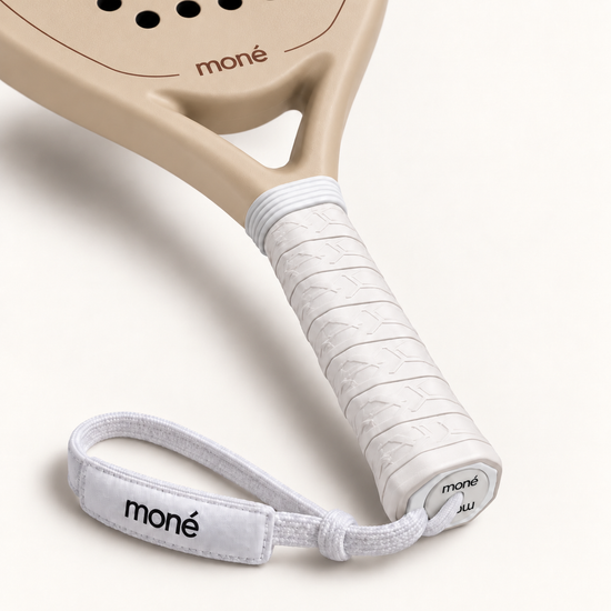 Close-up of the white textured grip, logo end cap and moné wrist strap on the beige Sahara Hybrid padel racket