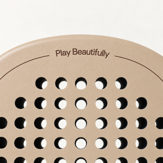 Top of the beige Sahara Hybrid padel racket face, with the Play Beautifully print above its drilled hole pattern