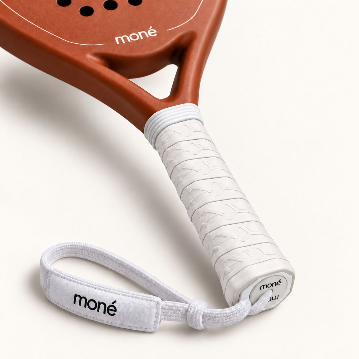 White textured grip, logo end cap and moné wrist strap on the light brown Sienna Hybrid padel racket, close-up