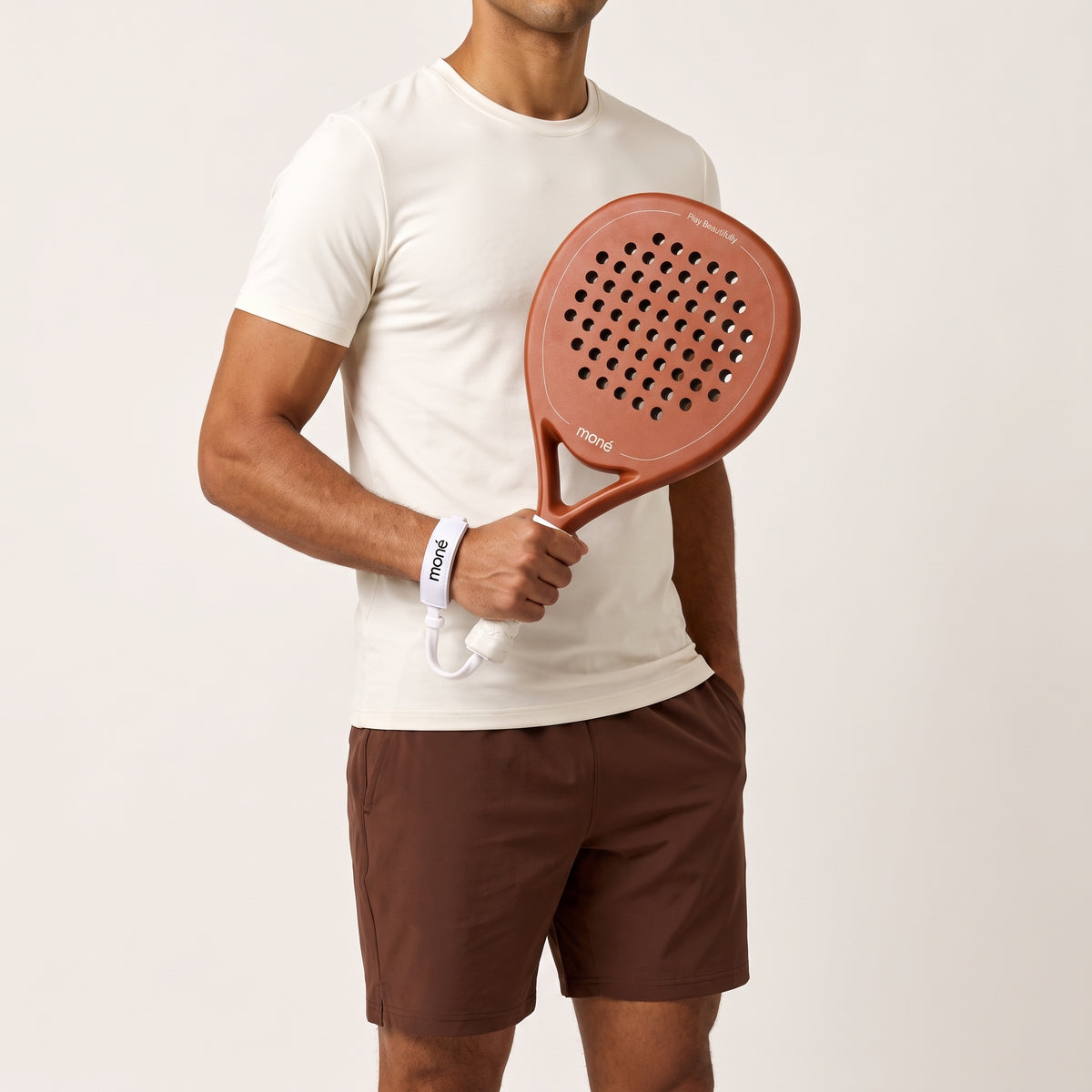 A man in a cream T-shirt and brown shorts holds the Sienna Hybrid padel racket in light brown against a light backdrop