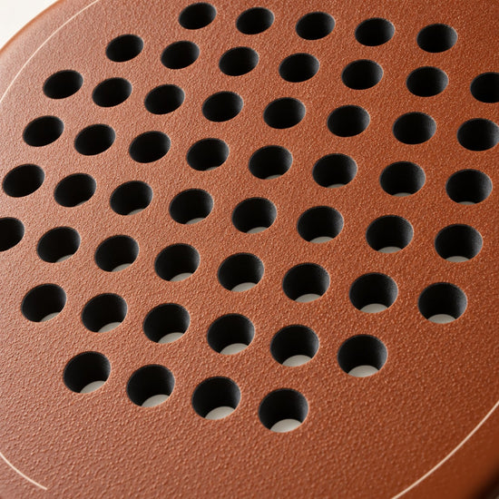 Rough, grainy light brown surface of the Sienna Hybrid padel racket in macro, textured around the holes to help spin