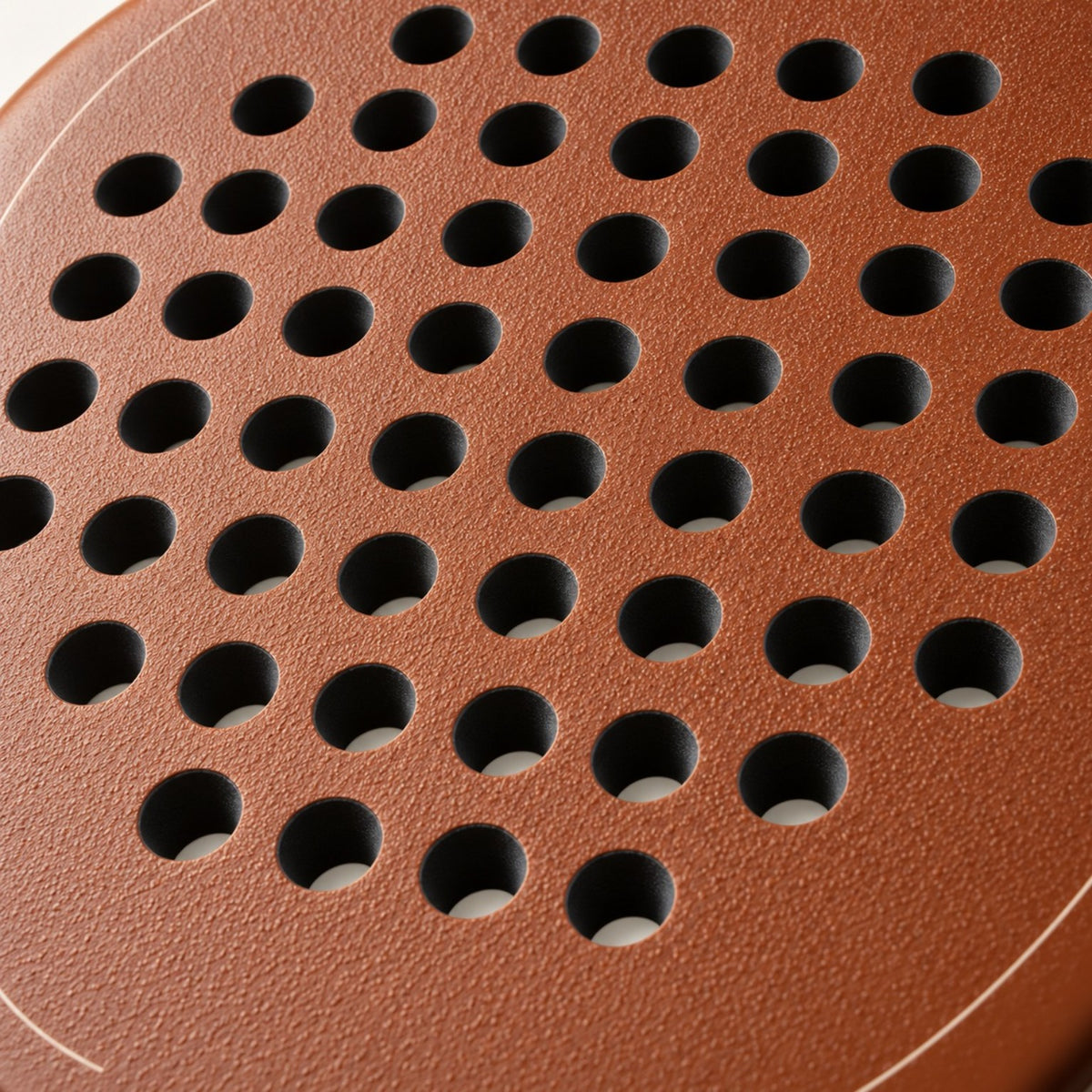 Rough, grainy light brown surface of the Sienna Hybrid padel racket in macro, textured around the holes to help spin