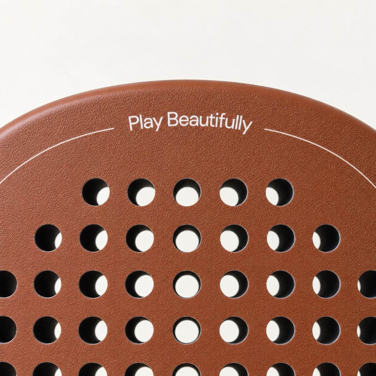 Play Beautifully printed in cream at the top of the light brown Sienna Hybrid padel racket, above its hole pattern